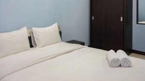 Ein ordentlich bezogenes Bett mit weißen Leinen und Kissen, ein dunkler Holzschrank und ein Paar zusammengerollte Handtücher auf dem Bett.