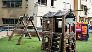 Ein Spielbereich für Kinder mit einer hölzernen Kletterkonstruktion und Rutschen, umgeben von einem grünen Rasen.
