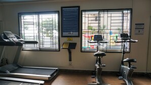Ein Fitnessraum mit Laufbändern und Ergometer, großen Fenstern mit Metallgitter und einer Wandtafel mit Informationen.