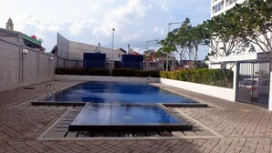 A swimming pool with a diving board, surrounded by a paved area and a gated entrance. - Comfortable And Warm 2Br At Tifolia Apartment (Jakarta)
