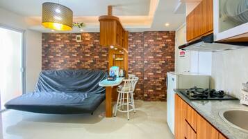 Un espacio habitable compacto con sofá, una pequeña mesa de comedor con sillas, una zona de cocina con estufa y una lámpara colgante.