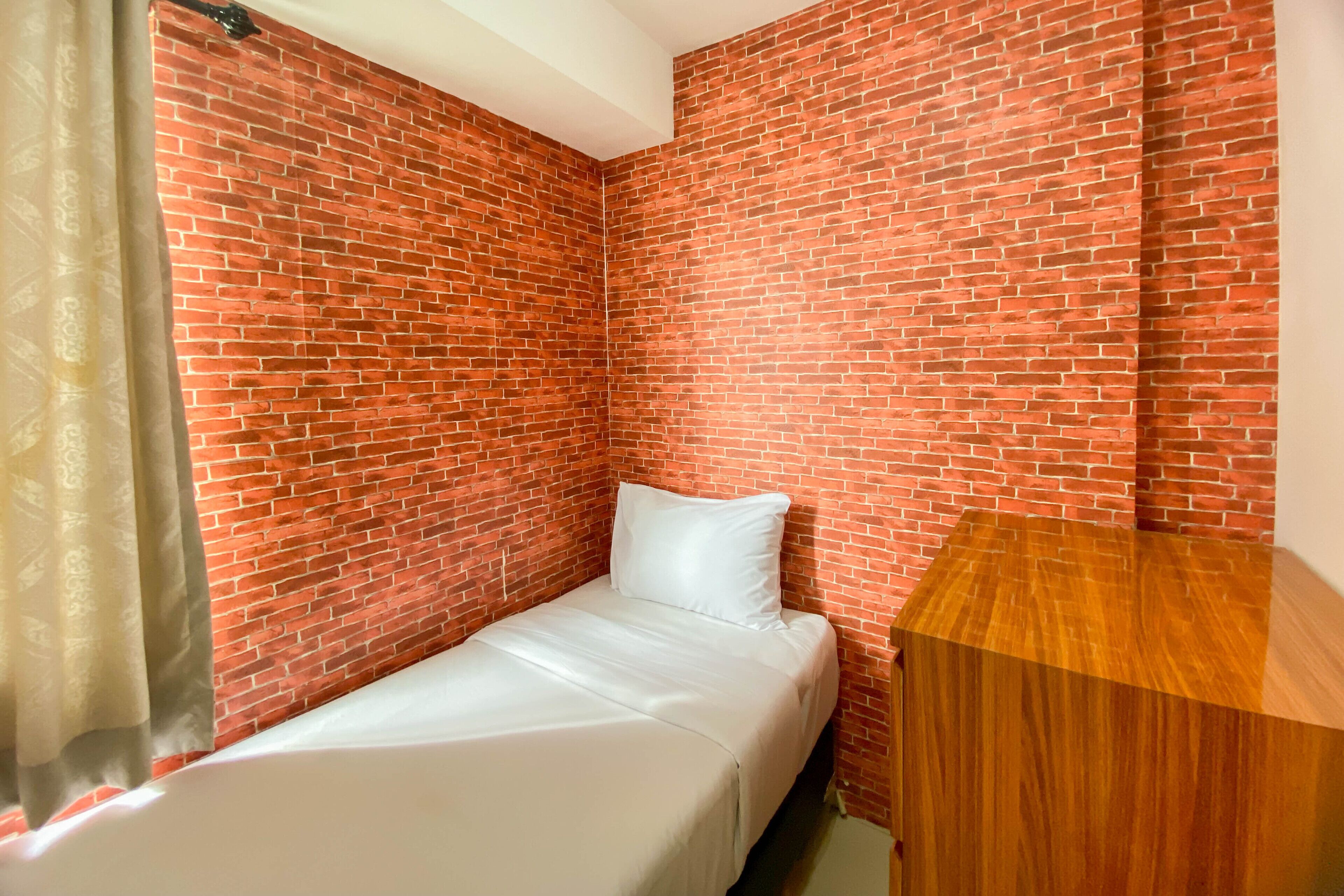 A small, single-bed room with a brick-patterned wall, a wooden nightstand, and a white bedspread.