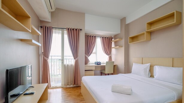 A hotel room with a bed, a desk, a chair, a TV, and a window with curtains. - Cozy Stay And Warm Studio Apartment At Margonda Residence 5 (Depok)