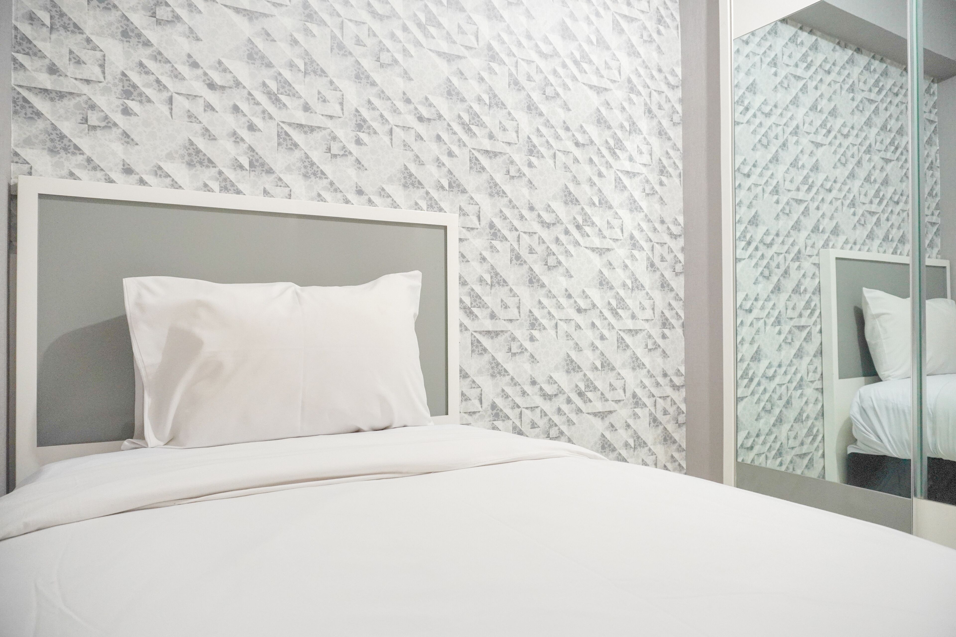 Une chambre d’hôtel moderne avec un mur orné d’un motif géométrique, un grand lit avec une literie blanche et une cloison en verre.