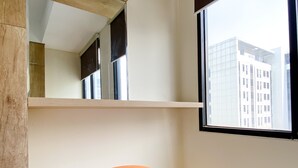Un coin de pièce avec une grande fenêtre, une étagère en bois et un pouf orange rond.