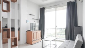 A modern living room with a sofa, a TV, a wooden cabinet, and a balcony with curtains. - Nice And Comfort 1Br At Citralake Suites Apartment (Jakarta)