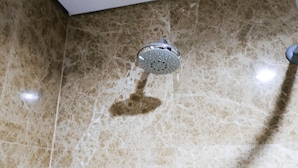 A showerhead on a marble floor with a visible water stain.