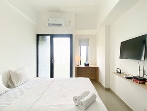 Habitación de hotel con cama, televisor montado en la pared, escritorio con lámpara y unidad de aire acondicionado.
