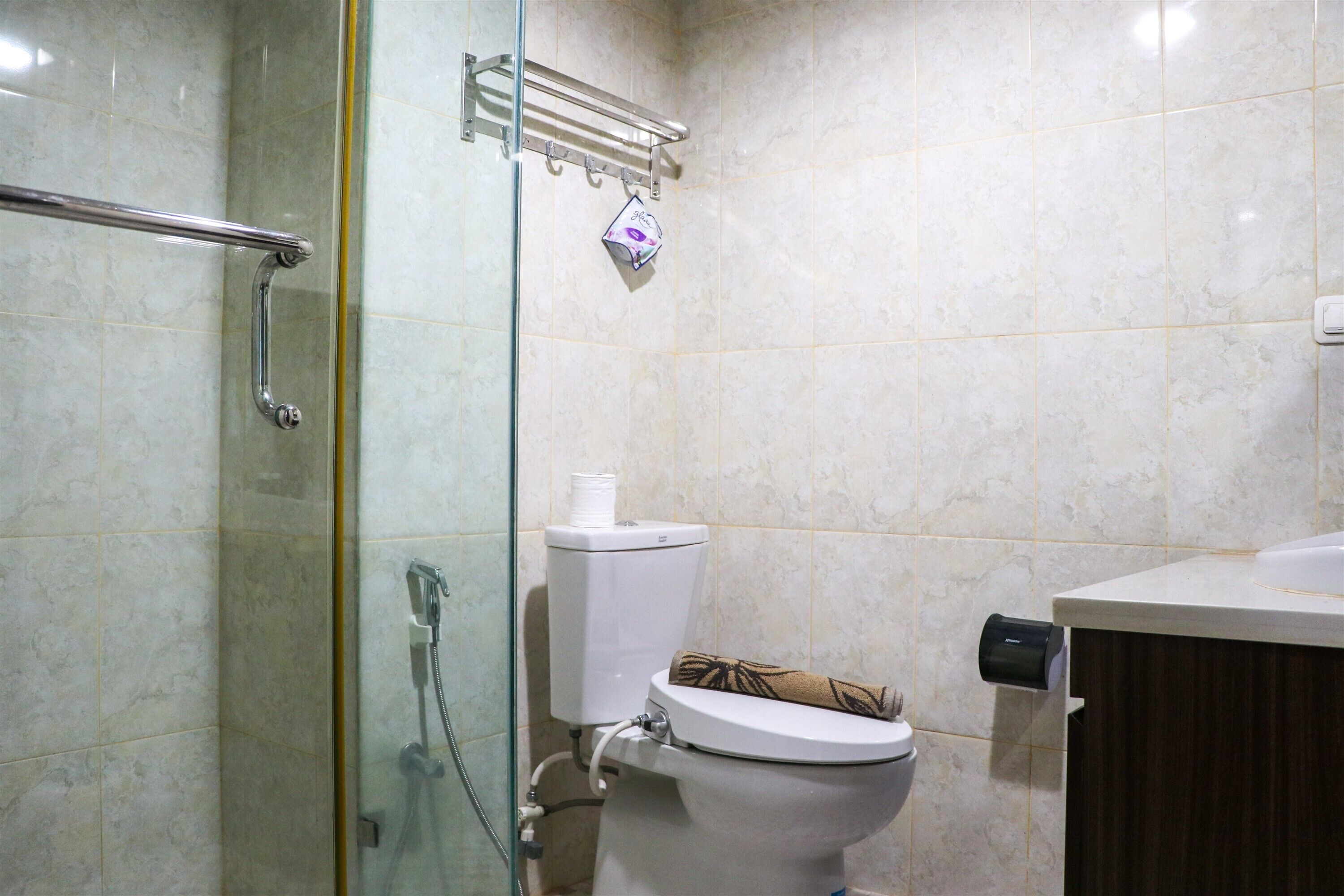 A bathroom with a glass shower enclosure, a toilet with a towel, and a paper towel dispenser.
