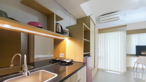 A modern kitchen with a stainless steel sink, a countertop with a kettle, and a built-in oven. There is a dining area with a white chair and a TV. - Luxury Studio At Taman Melati Sinduadi Apartment (Pogung Lor)
