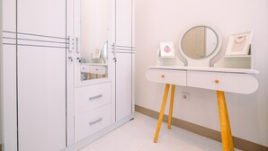 Une coiffeuse blanche avec un miroir rond, un tableau encadré et une petite étagère.