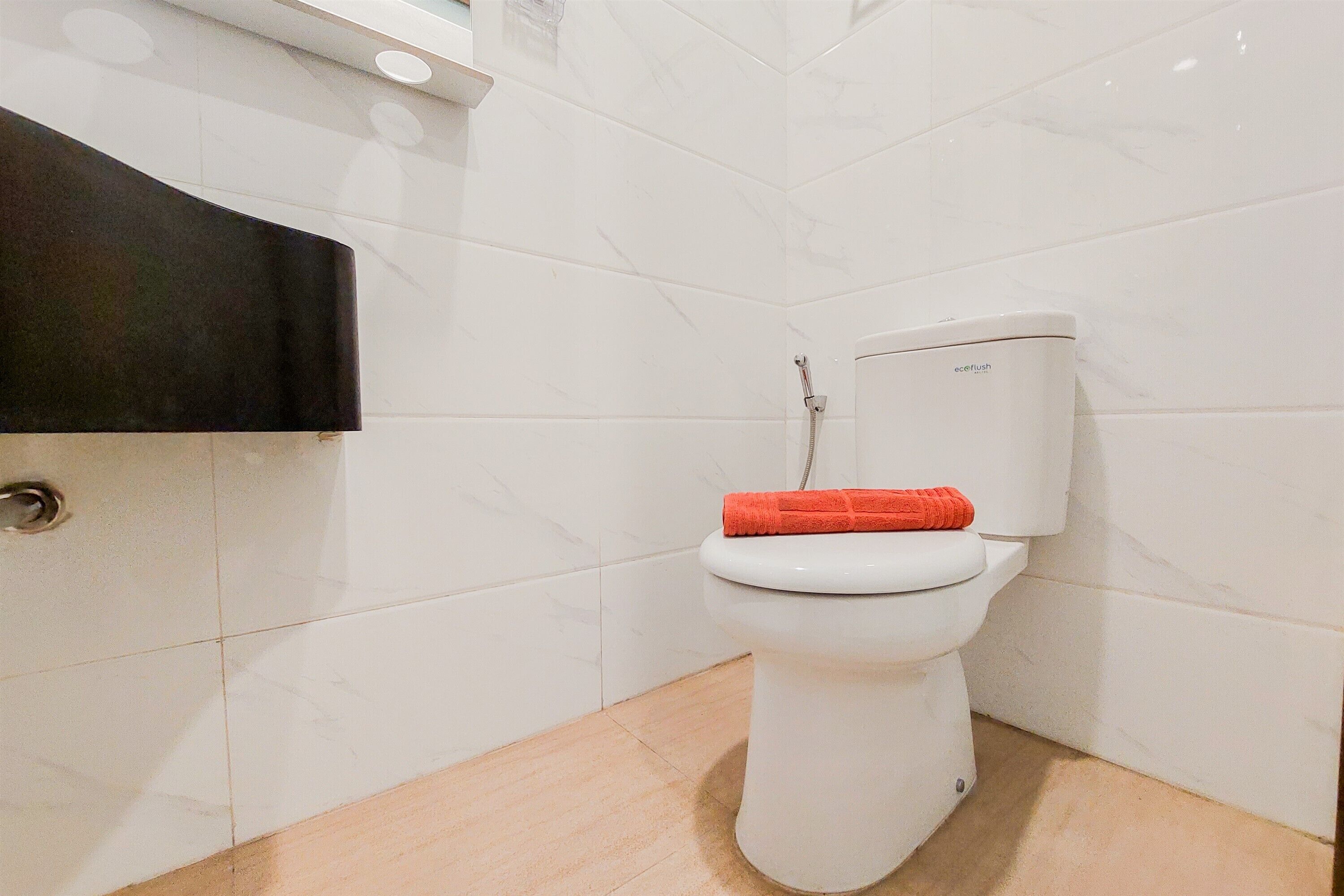 Eine weiße Toilette mit einem roten Handtuch darauf, einem schwarzen Handtuch an einem Halter und einem weißen Toiletttank.