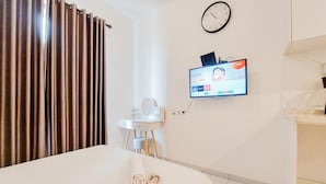 A hotel room with a bed, a TV mounted on the wall, a clock, and a bathroom vanity. - Simply And Nice Studio At Sky House Alam Sutera Apartment (Tangerang)