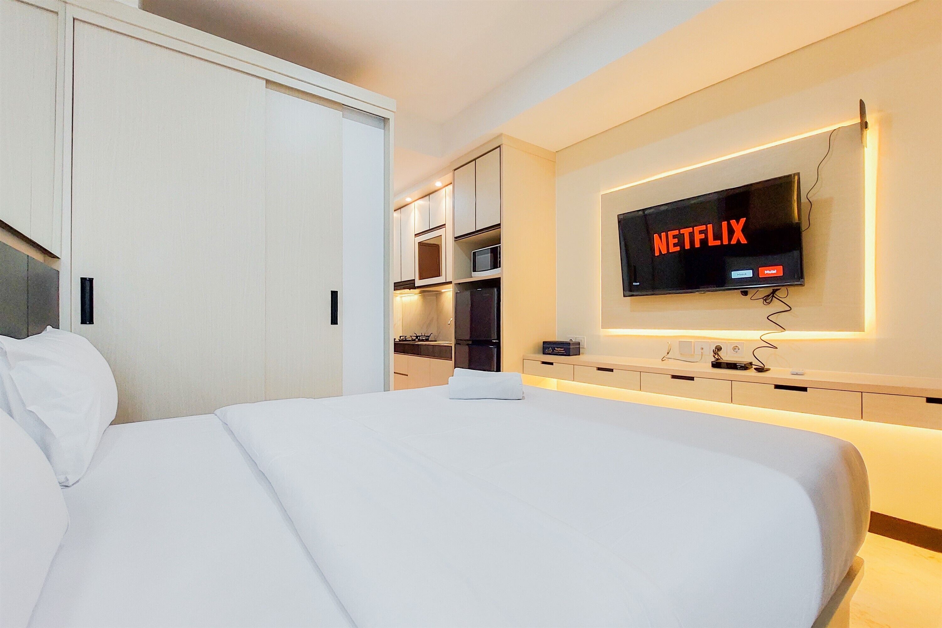 Habitación de hotel con cama, televisor montado en la pared y una zona de kitchenette.