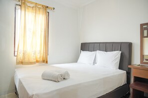 A neatly made bed with white linens and pillows, a wooden nightstand with a mirror, and a window with sheer curtains. - Best Homey 2Br Apartment Mediterania Palace Residence (Jakarta)