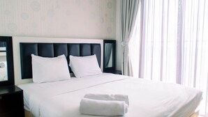 Un lit bien fait, avec du linge de lit blanc et deux oreillers, une serviette blanche pliée posée sur le lit, et une table de chevet avec une lampe sur le côté gauche.