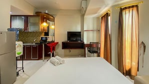 A hotel room with a bed, a desk, a TV, a minibar, and a kitchen area. - Comfort And Well Designed Studio Tamansari Sudirman Apartment (Jakarta)