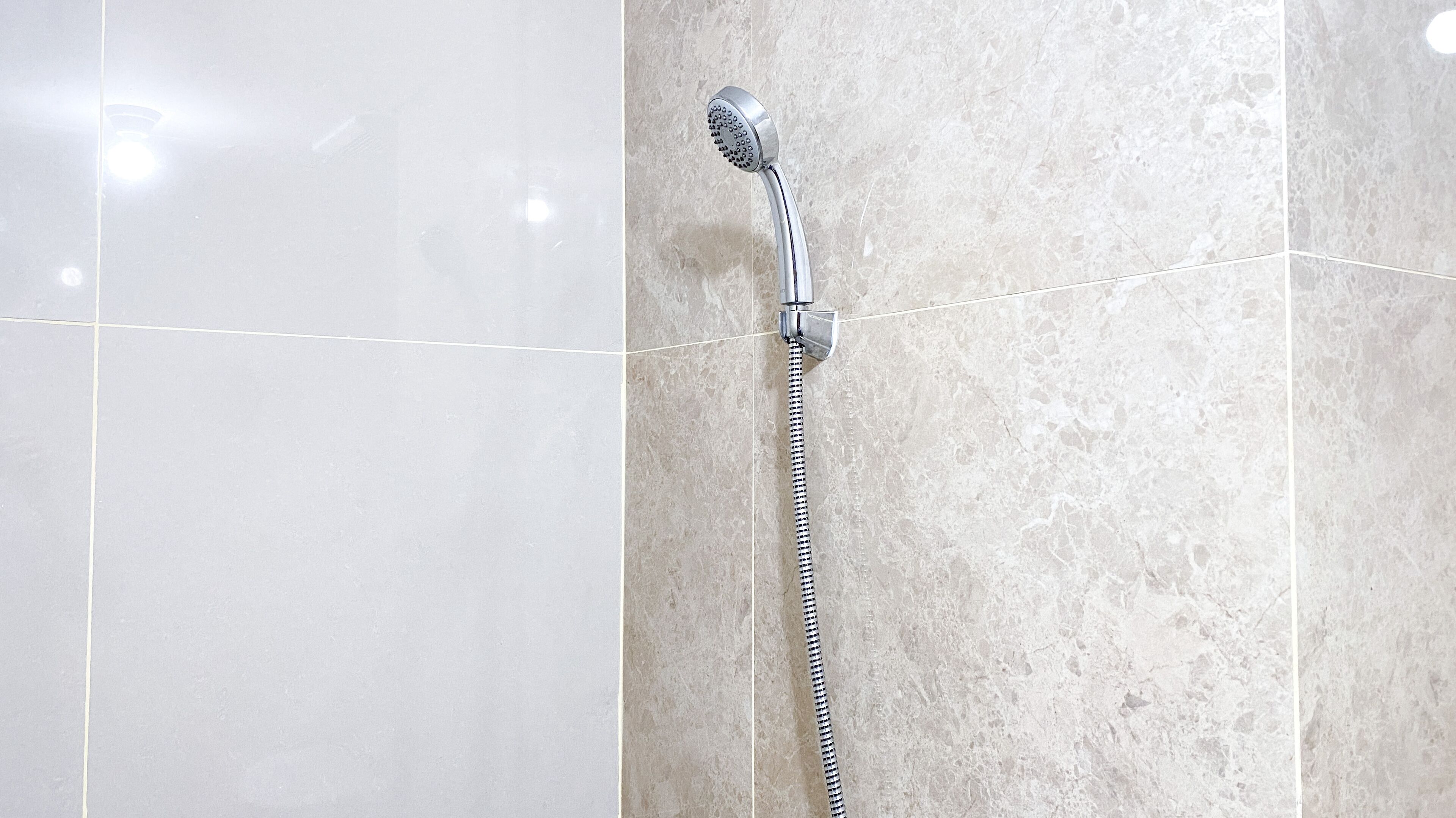 Un cabezal de ducha con una manguera flexible unida a una pared con textura similar al mármol.