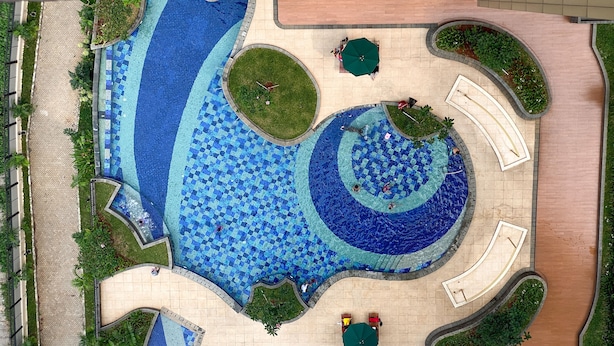 Una gran piscina al aire libre de varios niveles y formas, rodeada de zonas ajardinadas y senderos.