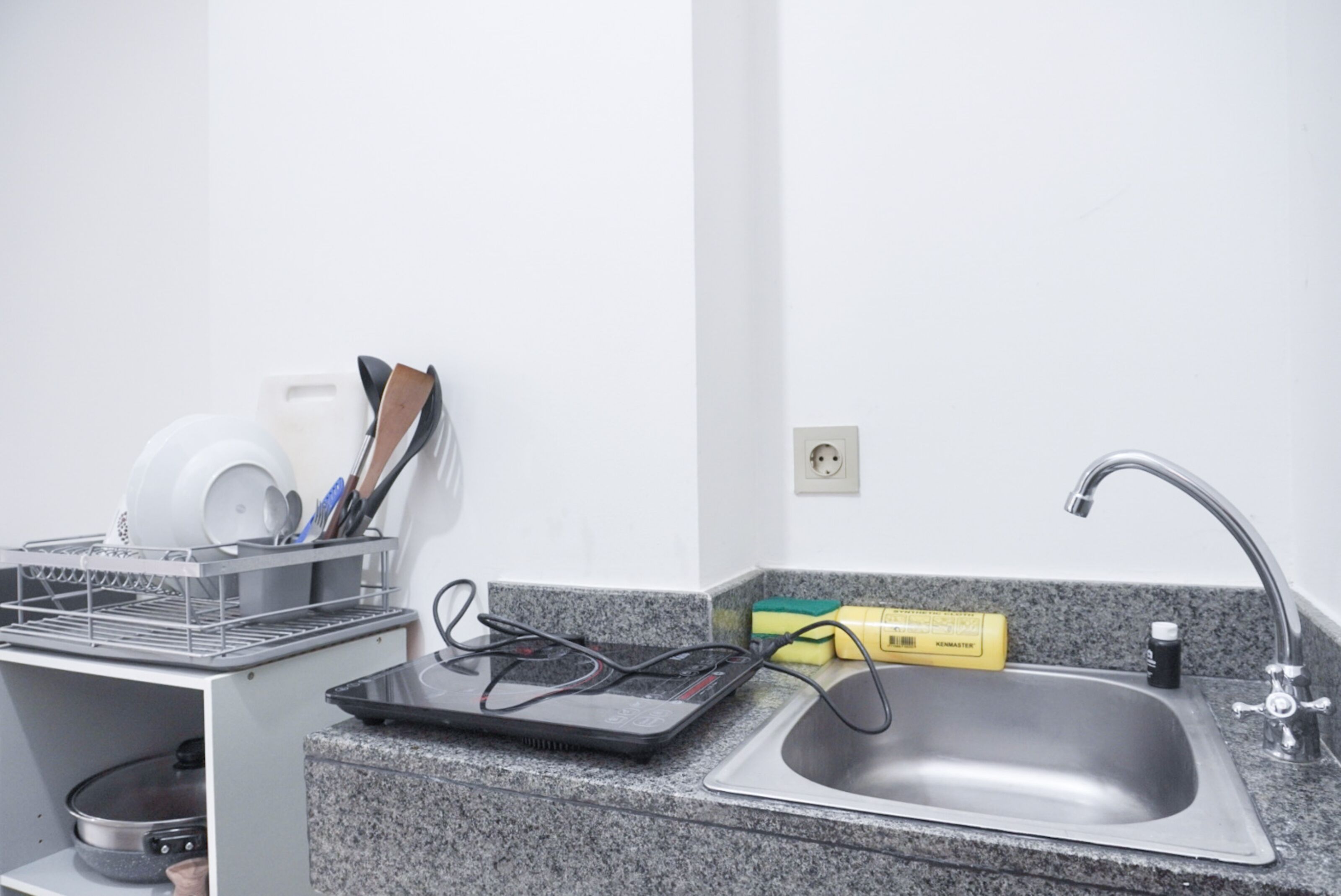 A kitchen with a granite countertop, a stainless steel sink, a dish rack, and a power strip.