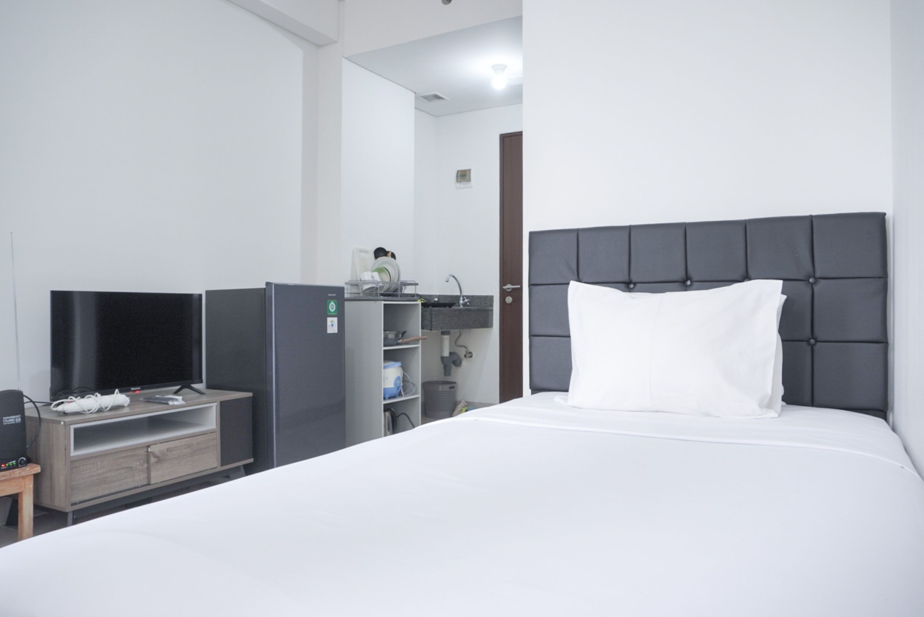 A hotel room with a bed, a television, a refrigerator, and a small table.