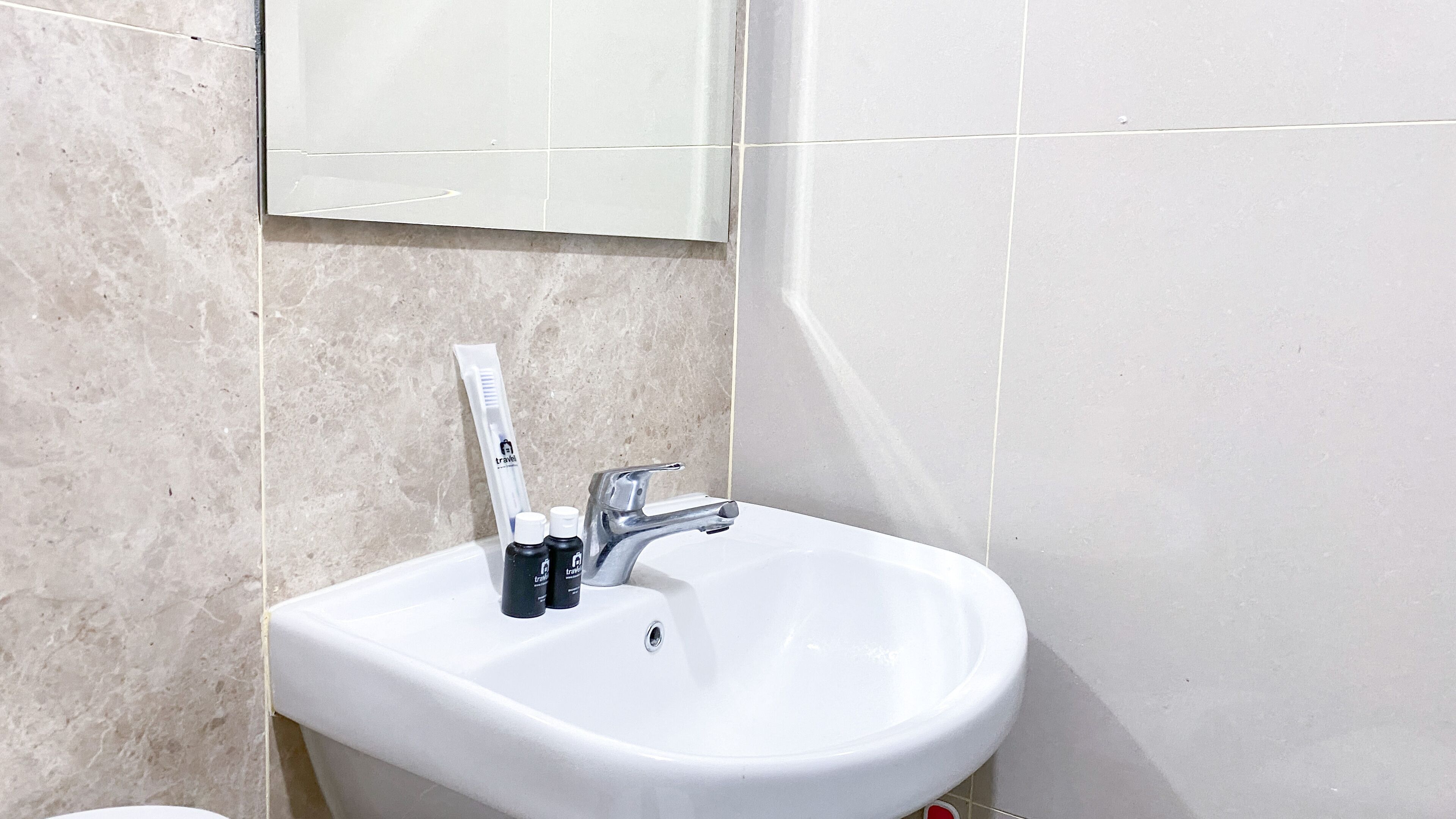 Een badkamer met een witte wastafel, een spiegel erboven en toiletartikelen op de wastafel.