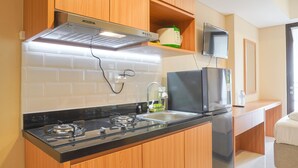 A compact kitchen with wooden cabinets, a gas stove, a microwave, and a built-in oven. - Nice And Elegant Studio At Vasaka Solterra Apartment (Jakarta)