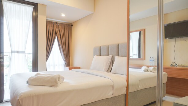 A hotel room with a large bed, a bedside table, a mirror, and a window with curtains. - Nice And Elegant Studio At Vasaka Solterra Apartment (Jakarta)