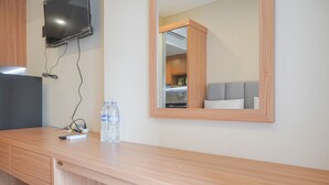 A wooden desk with a flat-screen TV, a water bottle, and a power strip. - Nice And Elegant Studio At Vasaka Solterra Apartment (Jakarta)