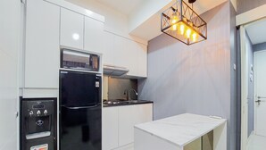 A modern kitchen with white cabinetry, a black refrigerator, a built-in oven, and a small island with a white countertop. - Comfortable And Minimalist 1Br At The Ayoma Apartment (South Tangerang)