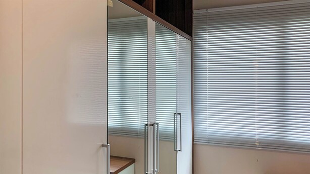 A room with a sliding glass door leading to a balcony, white walls, and a window with horizontal blinds.