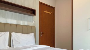 A bedroom with a bed, a wooden door with a coat hook, and a light switch on the wall.