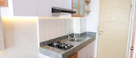 A compact kitchen with white cabinets, a granite countertop, a stove, and a sink.