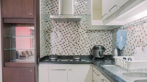 A kitchen with a gas stove, a kettle, and a coffee maker. There is a window with a view of a red building. - Spacious And Homey 2Br Mangga Dua Apartment (Jakarta)