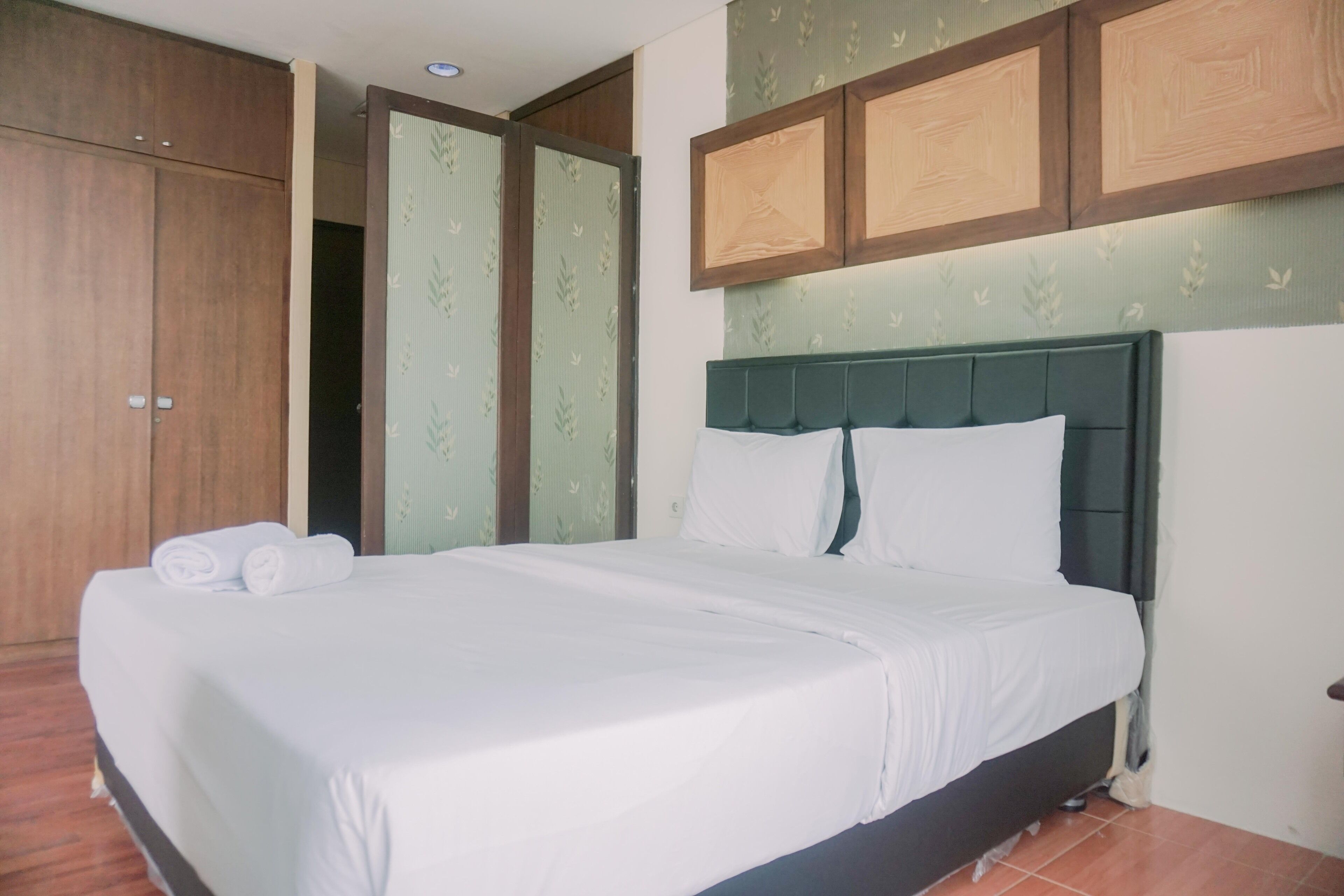 Uma cama bem arrumada com lençóis e almofadas brancas, um guarda-roupa de madeira e uma cabeceira estofada verde.