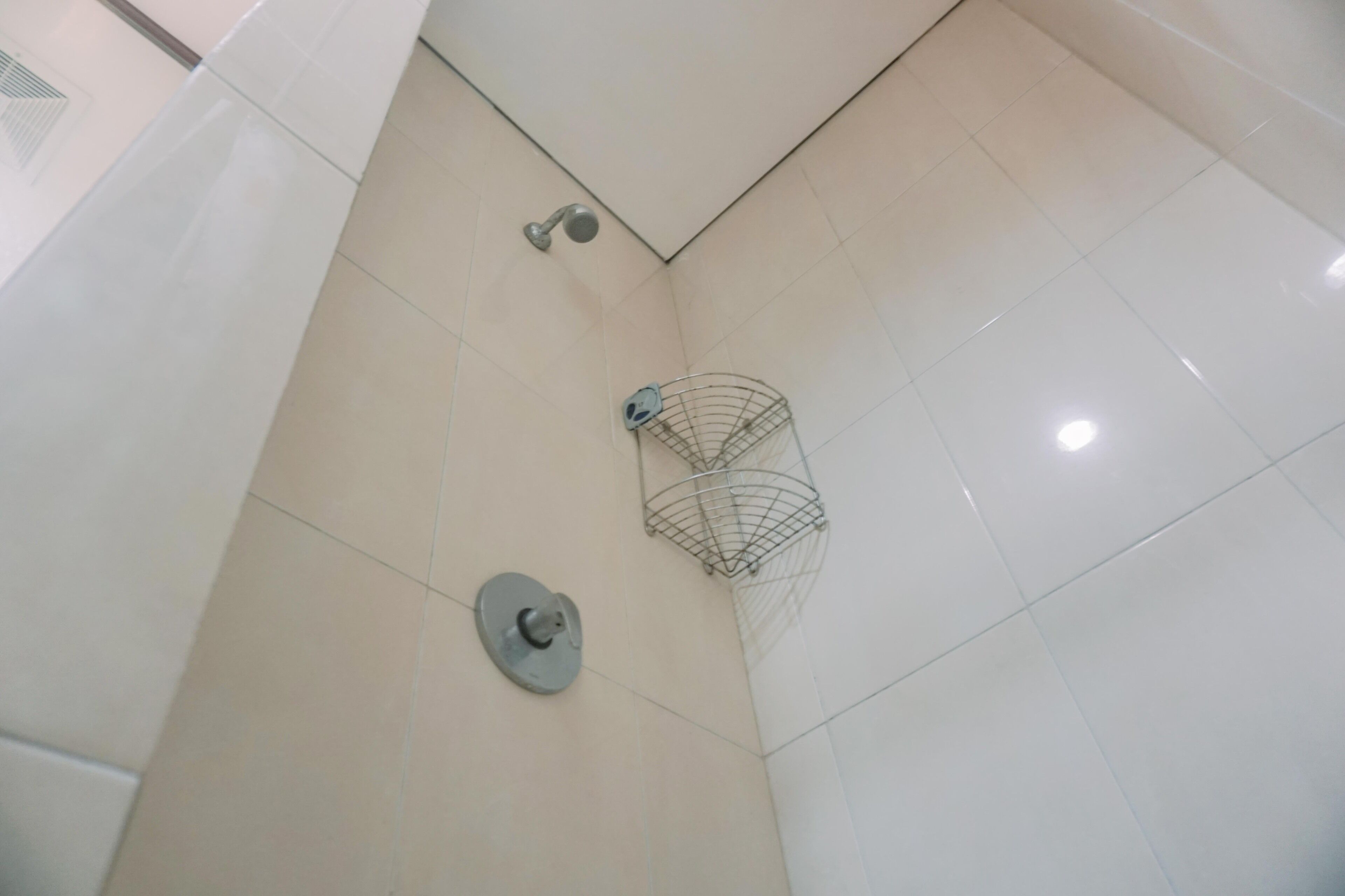 A corner of a bathroom with white tiles, a showerhead, and a metal shower caddy.