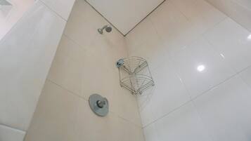 A corner of a bathroom with white tiles, a showerhead, and a metal shower caddy.