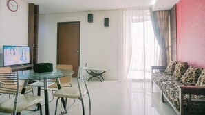 A modern living room with a glass table, chairs, a sofa, a television, and a door. - Spacious And Homey 2Br Mangga Dua Apartment (Jakarta)
