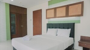 A neatly made bed with white linens and a green headboard, a wooden wardrobe, and a small wooden nightstand. - Spacious And Homey 2Br Mangga Dua Apartment (Jakarta)