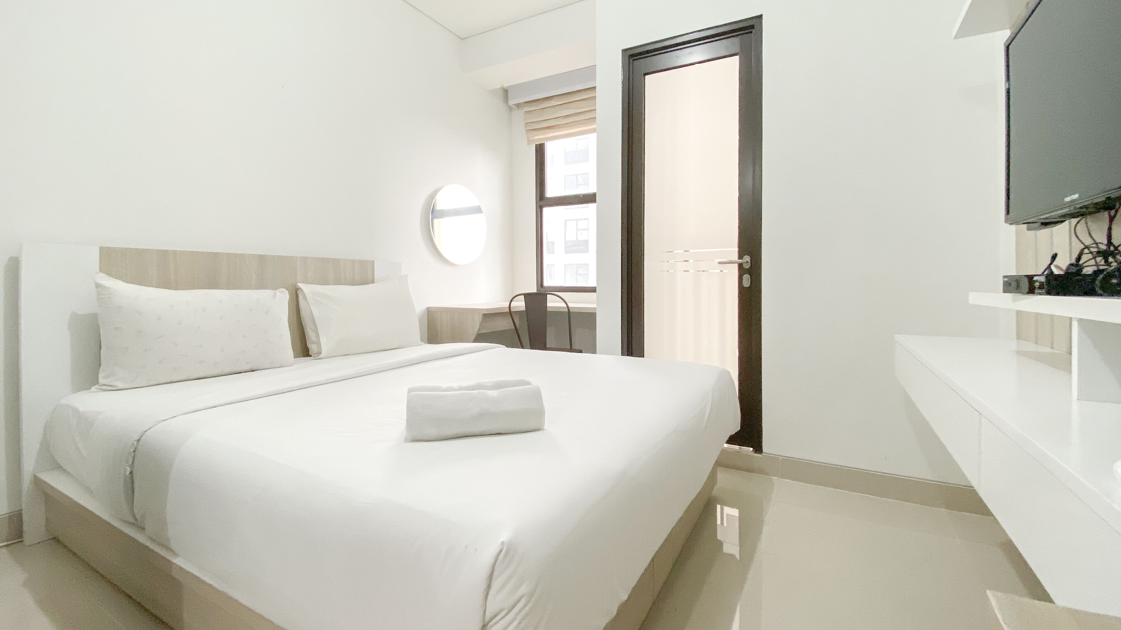 A hotel room with a bed, a chair, a television, and a window.