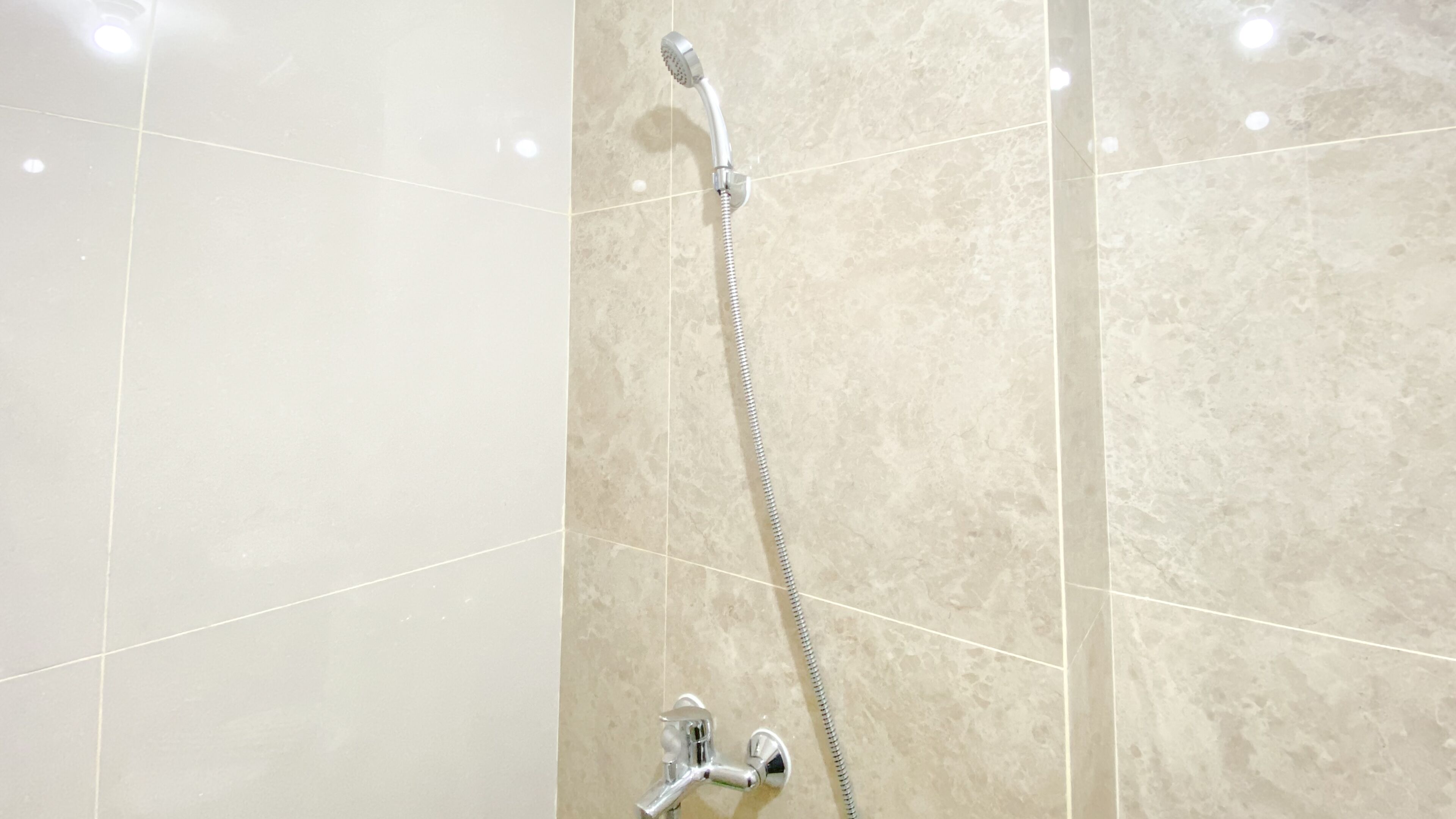Une douche équipée d’un pommeau de douche à main et d’un robinet fixé au mur.