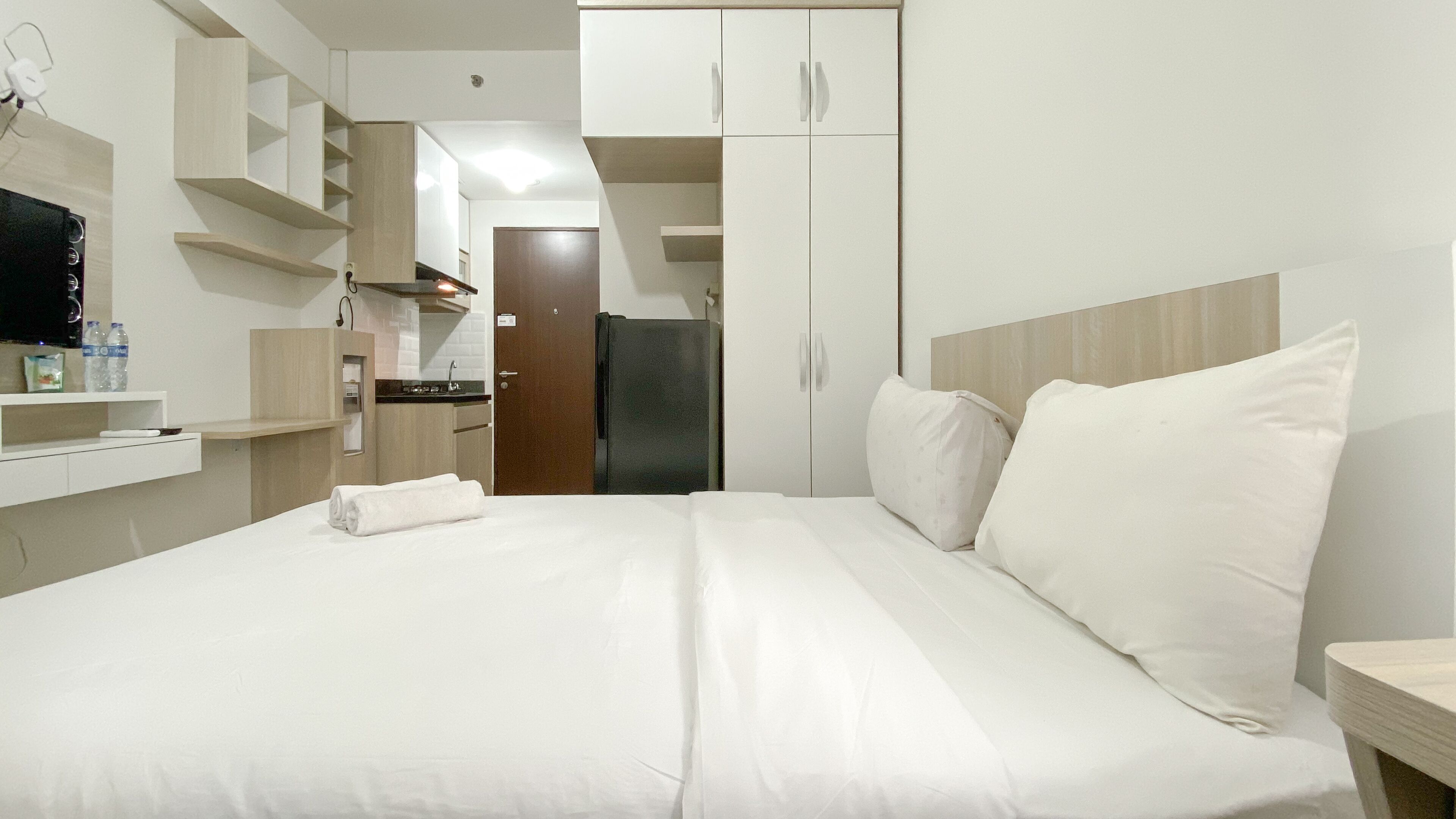Habitación de hotel con cama, mesita de noche, una pequeña mesa, espejo, armario y kitchenette.