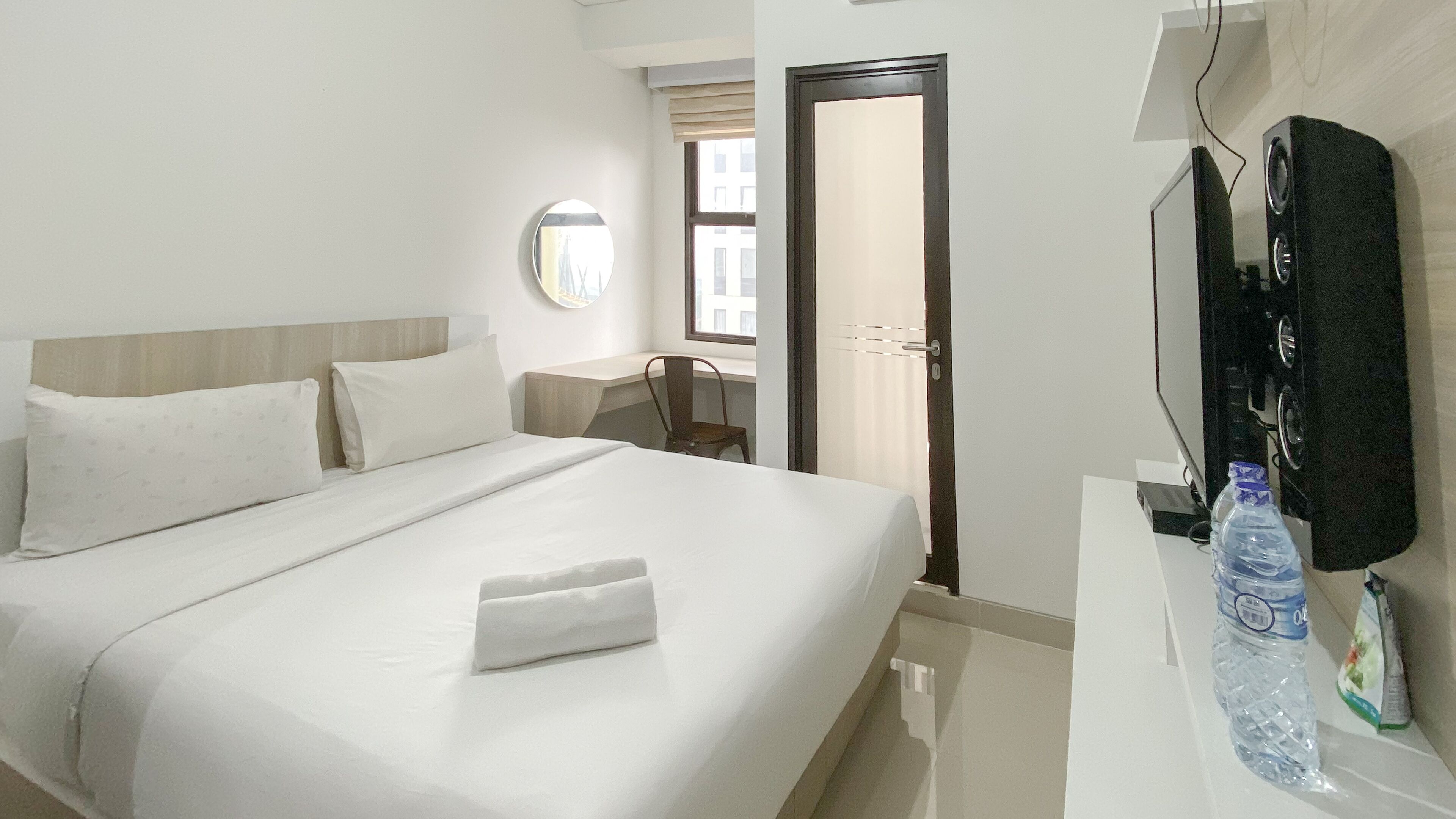 Een hotelkamer met een bed, een stoel, een televisie en een waterfles op het aanrecht.