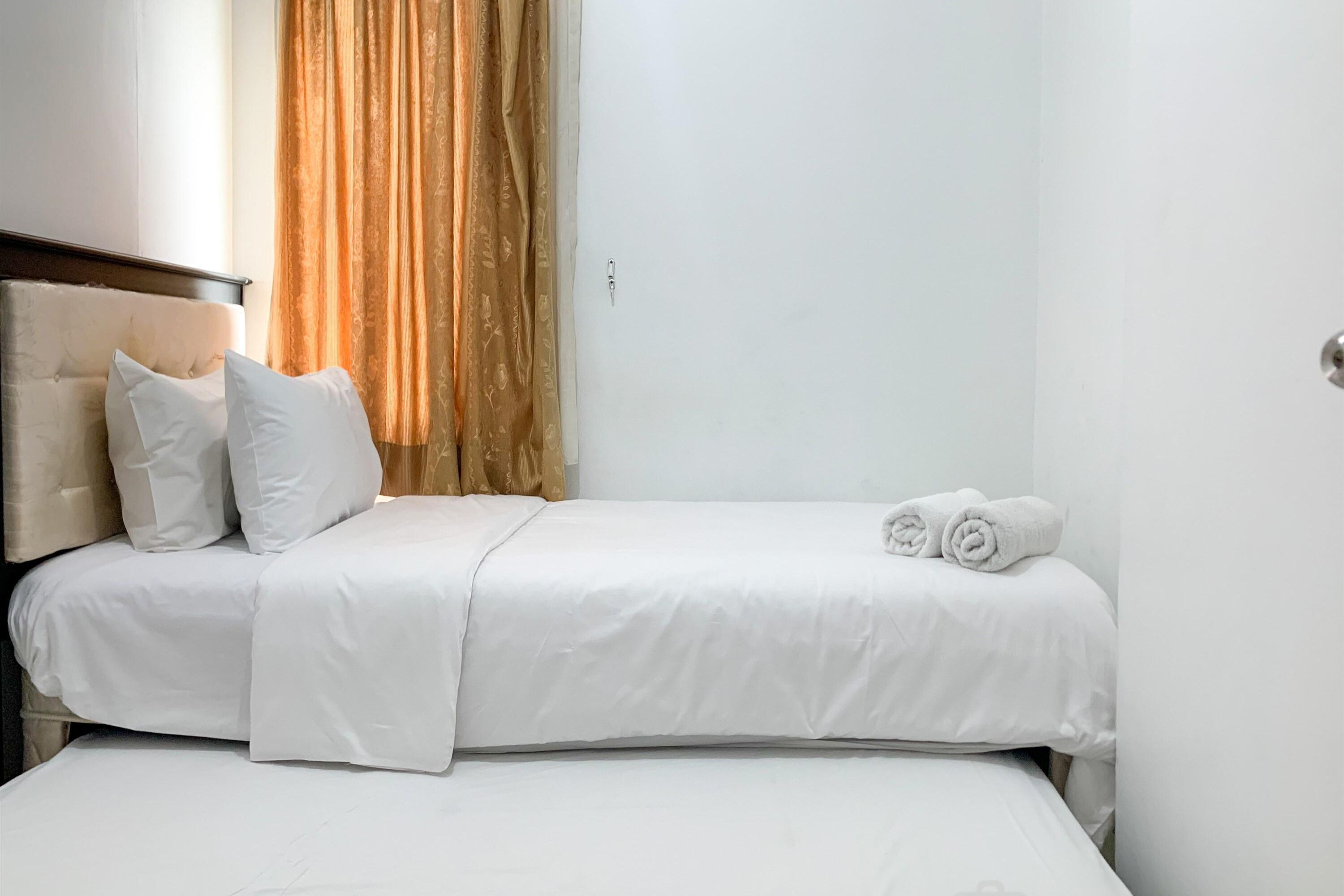 Quarto de hotel com cama, roupa de cama branca, duas almofadas e cortina.