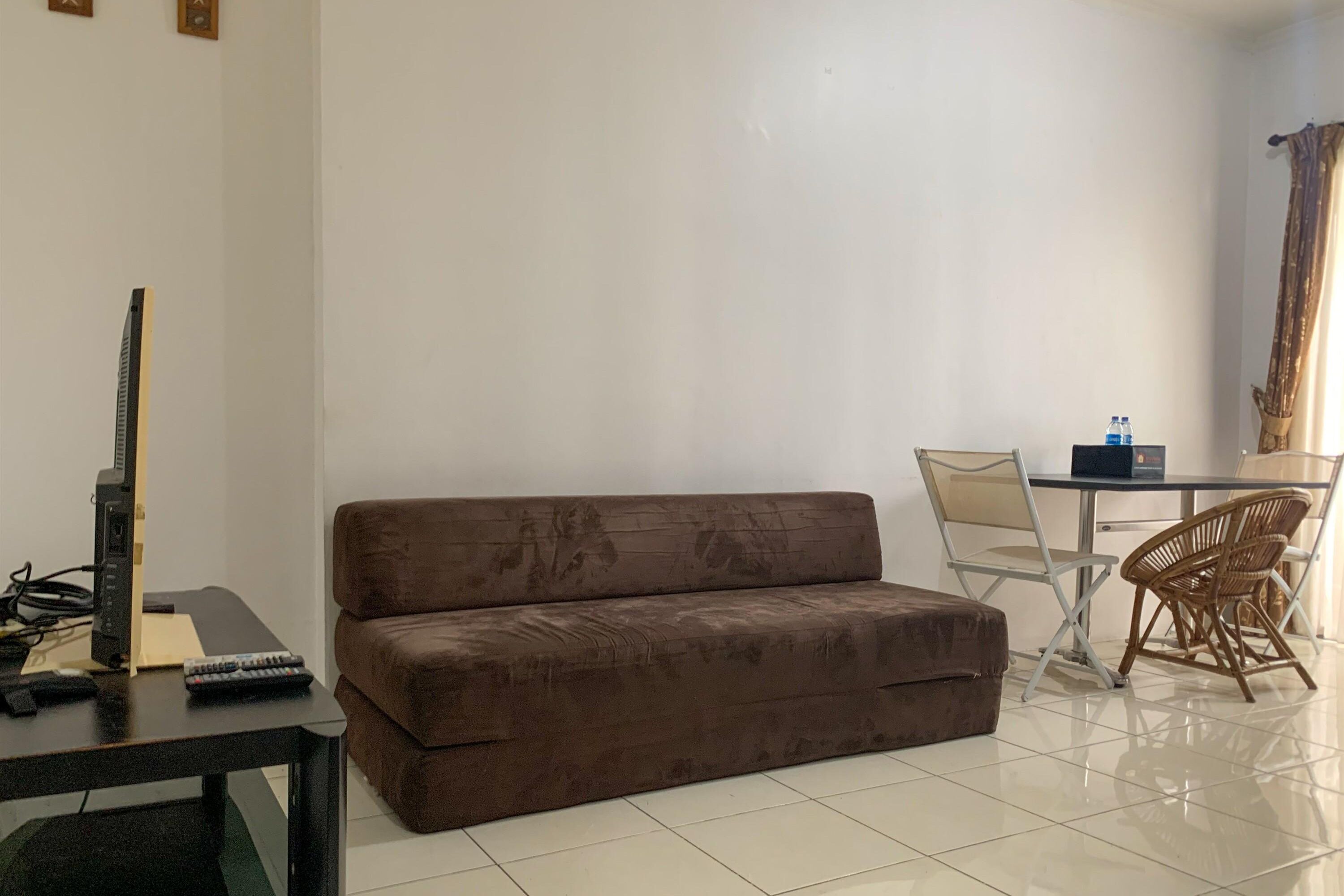 En stue med en brun sofa, et lille bord med fjernsyn og fjernbetjeninger, et spisebord med stole og en vandflaske på bordet.