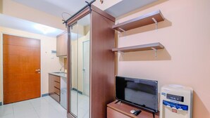 Quarto de hotel com porta deslizante, televisão de tela plana, minibar e dispensador de água.