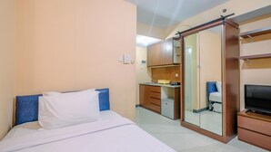 Quarto de hotel com cama, televisão, guarda-roupa e kitchenette.