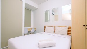 A neatly made bed with a rolled towel, a wooden wardrobe, and a desk with a chair. - Best Price Studio Room Transpark Cibubur Apartment (Depok)