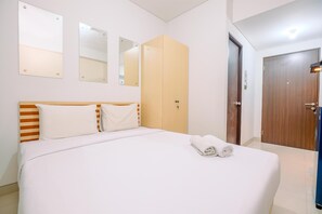 Quarto de hotel com uma cama grande, cabeceira de madeira, duas espelhos, um guarda-roupa e uma porta.