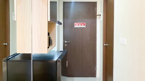 A hotel room with a wooden door, a black minibar, and a small shelf with a kettle. - Modern Look And Homey Studio Apartment At Transpark Juanda Bekasi Timur (Bekasi)